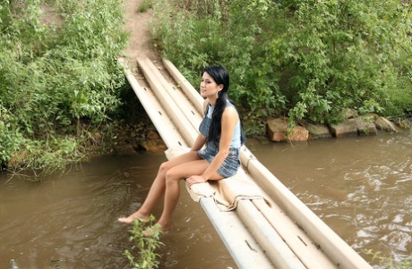 Chica de pelo oscuro y su amante follan en un puente de madera que cruza un arroyo