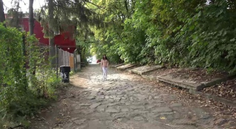 La jeune fille brune Dee baisse son legging blanc pour faire pipi derrière des buissons.