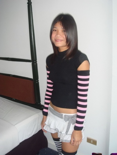 En knappt laglig asiatisk tonåring klär sig i lårhöga strumpor som matchar hennes armstrumpor