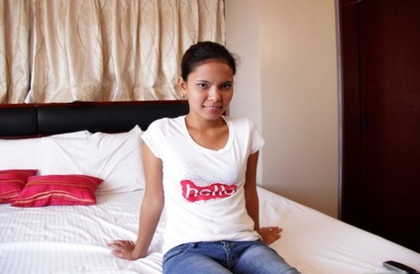 Asiatischer Teenager zieht vor dem Sex auf weißem Bettlaken ein T-Shirt und blaue Jeans aus