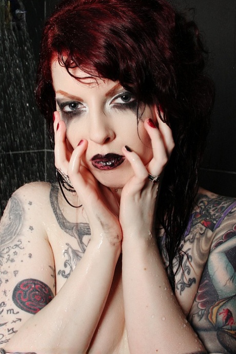La rousse tatouée Penny Poison prend des poses superbes sous la douche.