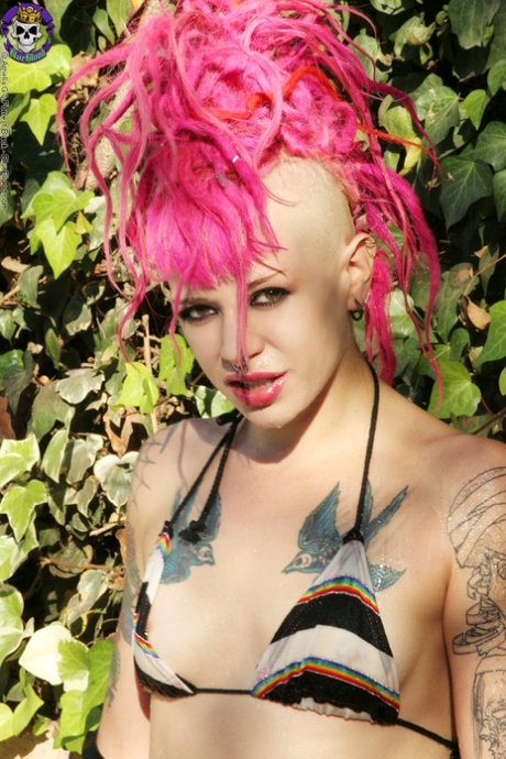 La punk tatuada Roxy Contin luce pelo rosa brillante mientras se desnuda en una piscina