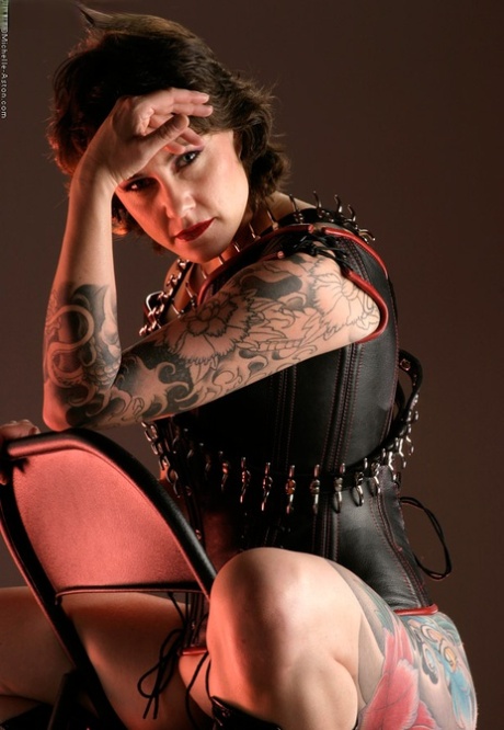 Tattooed brunette Michelle Aston shows her hairless pussy in fetish apparel