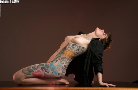 Mulher tatuada Michelle Aston bate em grandes poses semi-nus sobre uma mesa