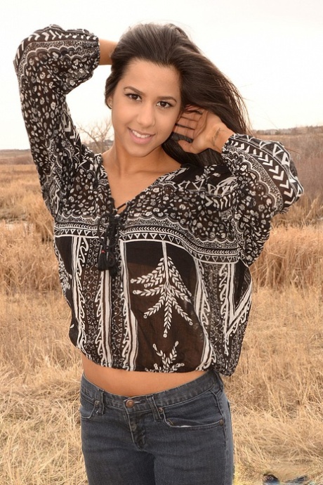 Den latinamerikanske jenta Bella Quinn står modell på et jorde i BH og jeans.