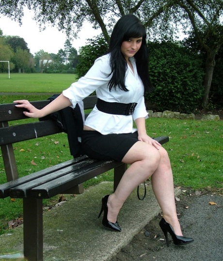 Ubrana modelka Nicola pozuje na ławce w parku, aby pokazać swoje seksowne nogi