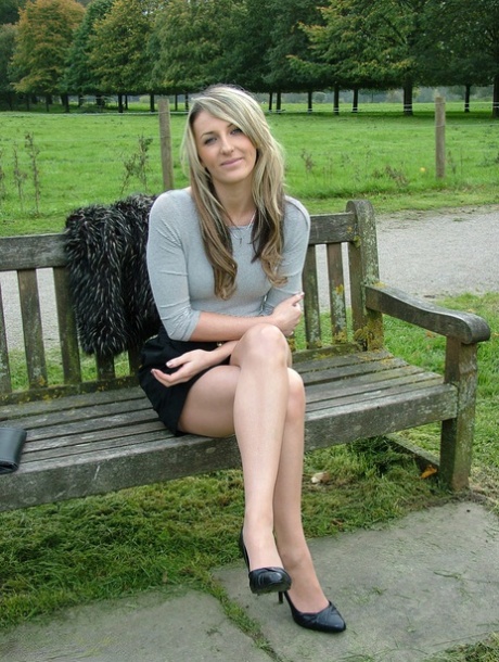 Un mannequin pose sur un banc de campagne en jupe noire et escarpins.