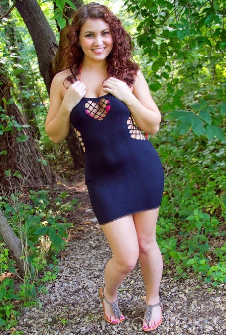 Gewelfd sexy meisje glijdt uit haar strakke jurk om haar tieten te laten zien in het bos