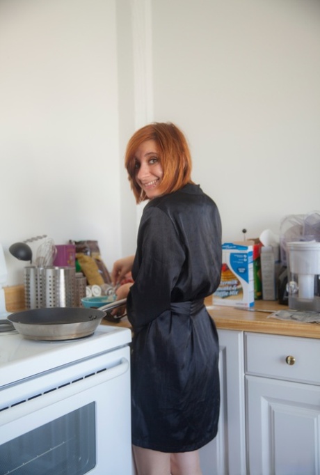 A amadora ruiva Chesea Bell guarda o seu roupão de cetim preto para cozinhar nua.
