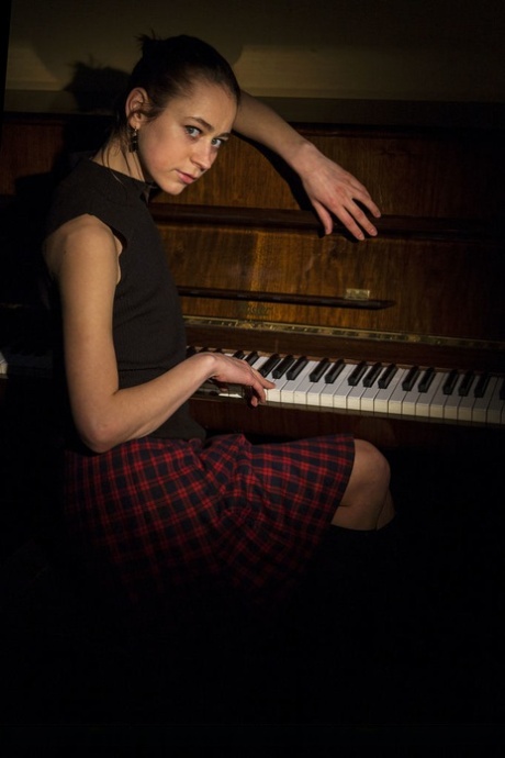 Slanke brunette Tigra poseert naakt op een piano.