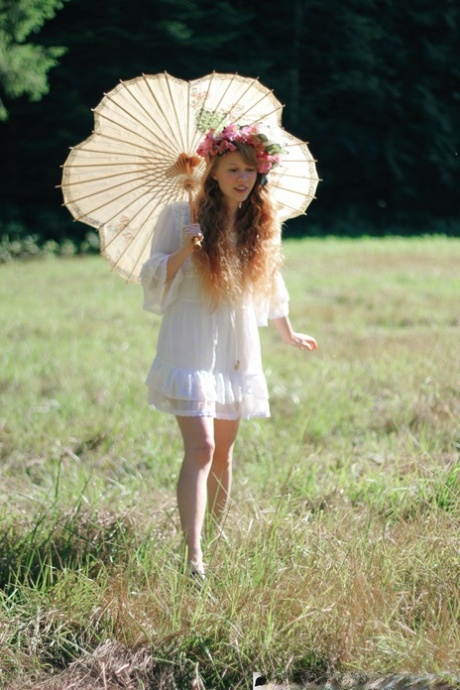 Charming redheaded teen Dolly Little holds a parasol while getting naked