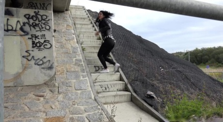 Das dunkelhaarige Mädchen Dee zieht ihre Leggings herunter, um auf einer Betontreppe zu pinkeln