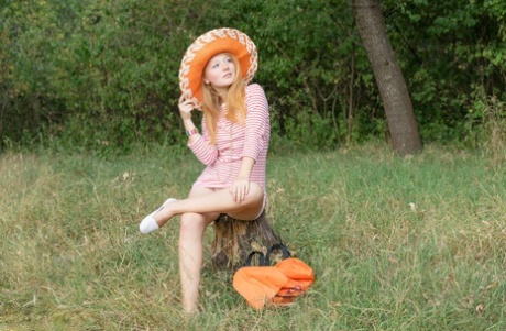 Young girl with red hair holds an orange while posing naked on a blanket