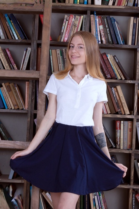 Cienka nastolatka pokazuje swoją bawełnianą bieliznę podczas przeglądania książek w bibliotece