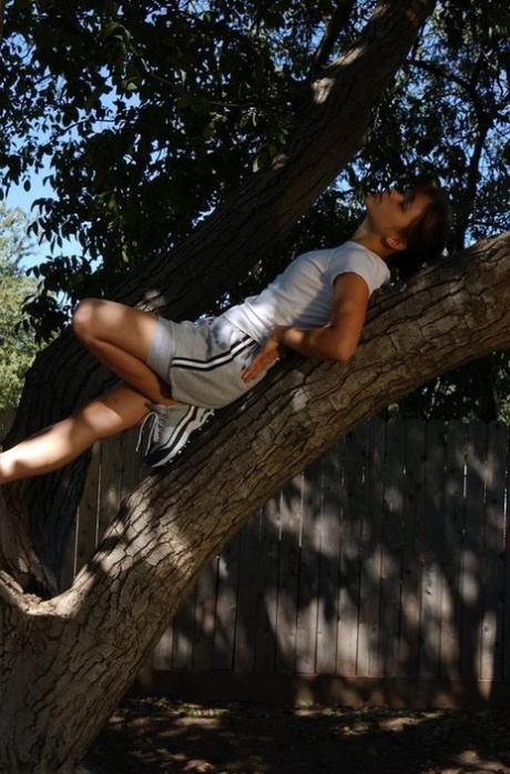 Petite teen Karma strips off her clothes to pose nude up in a tree