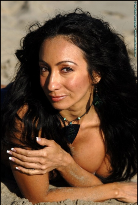 Modelo de fitness latino Monica Goe posa numa praia arenosa em fato de banho