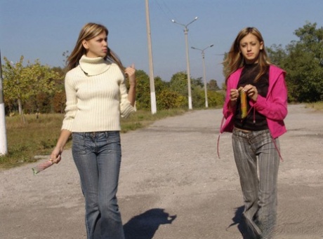 Blonde teens hold hands while licking frozen treats on a road