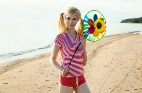 Jonge blonde Candy rukt aan haar staartjes na naakt op een strand