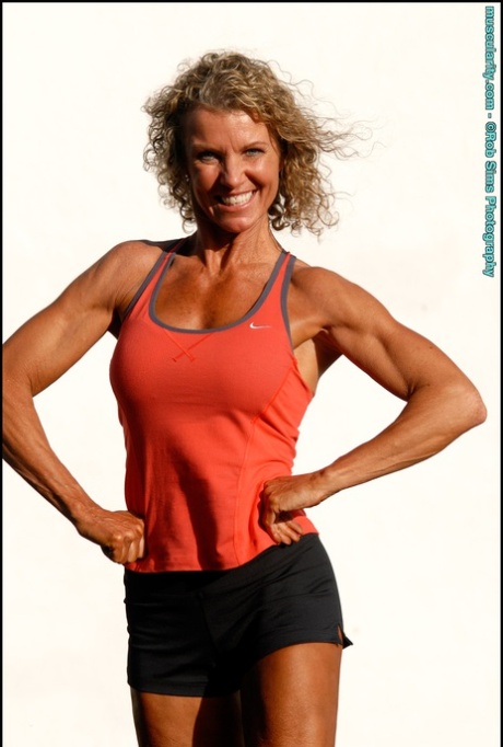 A fisiculturista Denise James desfila o cabelo encaracolado enquanto posa ao ar livre em biquíni