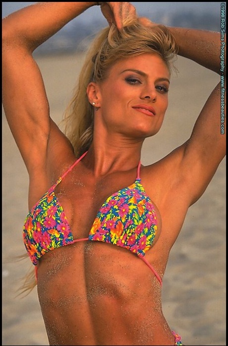 Blond fitnessmodel Sandy Jones poseert op een zandstrand in bikini