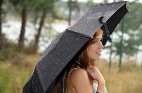 Horny young girl masturbates by a chain-link fence while holding an umbrella