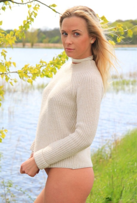 Den unge, blonde Cristal Caitlin løfter opp genseren mens hun står bunnløs ved en elv.