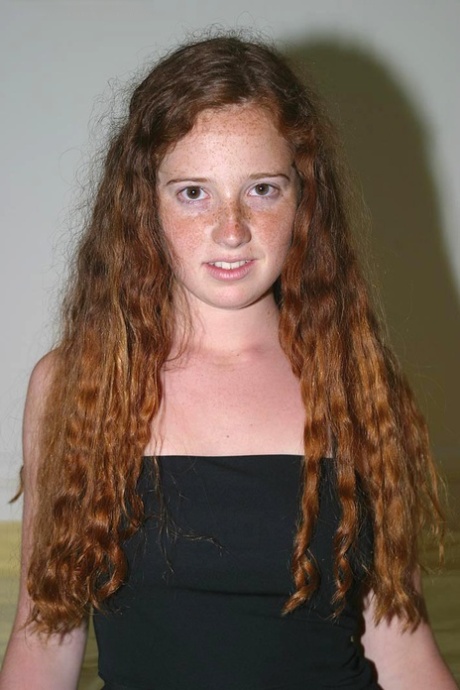 Una ragazza giovane con i capelli rossi ricci si spoglia completamente sul suo letto