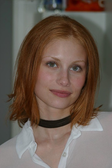 Anya, rousse et pâle, pose nue sur le comptoir de la cuisine avec un collier noir.