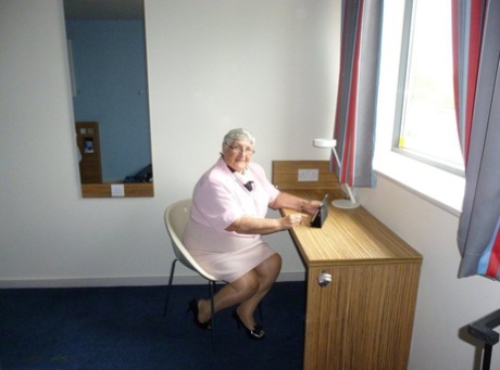 Übergewichtige alte Frau Oma Libby legt ihre schlaffen Titten auf einen Schreibtisch, während sie sich auszieht