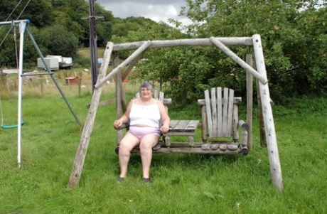 Oude Britse vrouw Oma Libby toont haar borsten op een schommelbankje in de achtertuin
