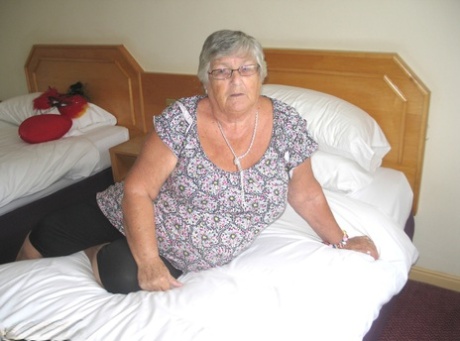 Silverhårig brittisk kvinna Grandma Libby exponerar sin feta kropp på en säng