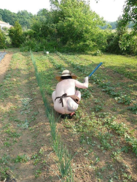 Mary Bitch, femme mûre, s'occupe de son jardin, nue, en chapeau de soleil et tablier.