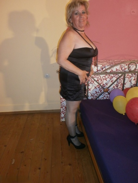 Sexy babička Caro v lesklých průsvitných punčochách a podpatcích drtí balónky na posteli