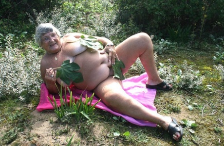 Den feta brittiska kvinnan Grandma Libby klär av sig naken på en handduk på en skrubbig mark