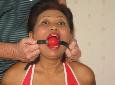 Mature Asian woman drools after being fitted with a ball gag while restrained