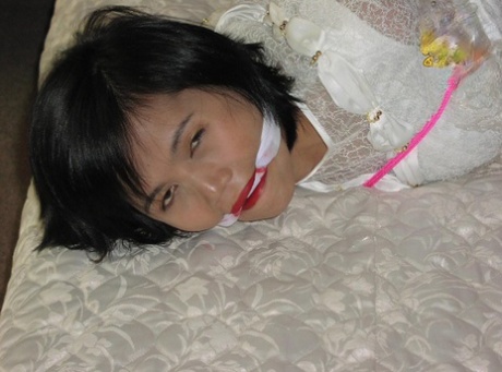 Azjatka jest zakneblowana podczas wiązania w ubraniu na łóżku
