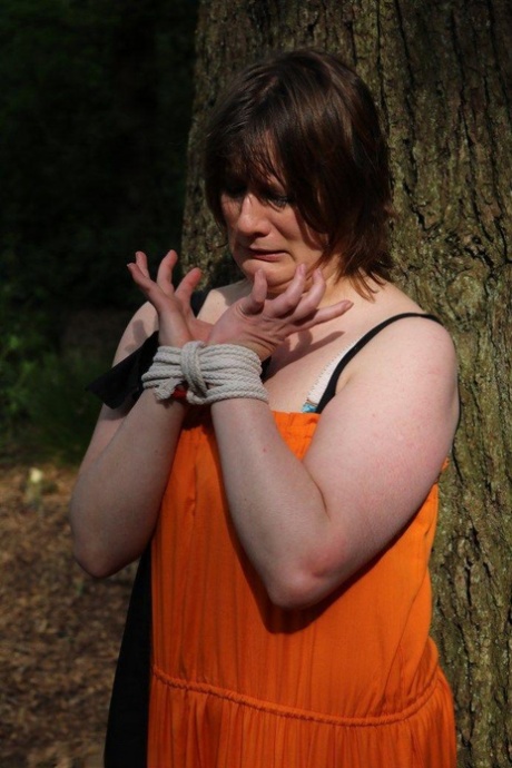 Fat female is gagged and tied to a tree in the woods with her clothes on