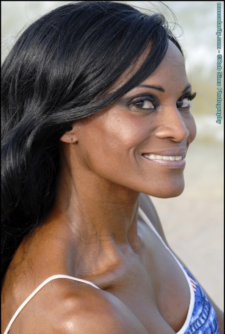 Black bodybuilder Debra Dunn flexes her muscles at the beach in denim attire