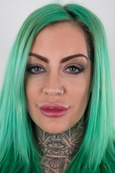 Tattooed girl with green hair and pierced nipples stands naked after disrobing