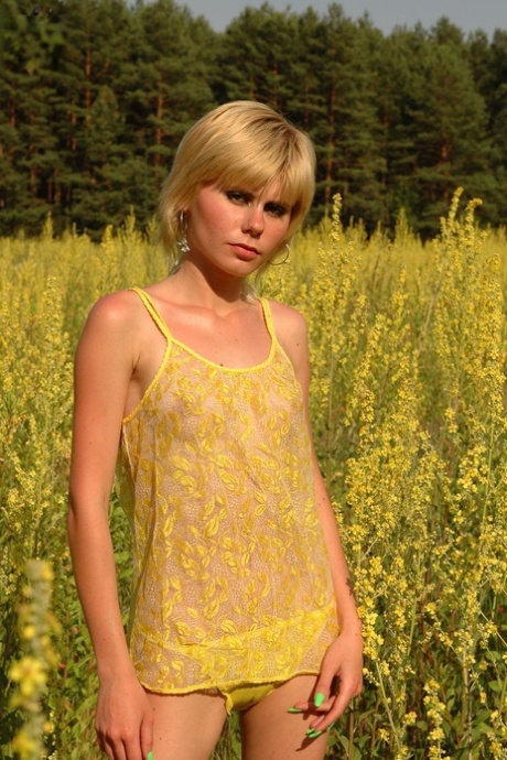 Jong kijkend blond meisje toont haar magere lichaam te midden van bloeiende wilde bloemen