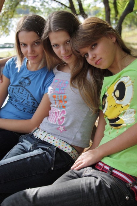 3 unge jenter tar av seg T-skjorter og jeans for å stå modell nakne på en parkbenk.