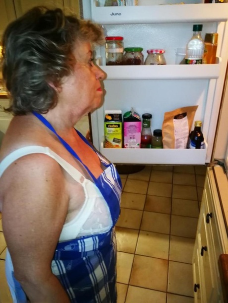 La vieja ama de casa Caro se quita la ropa interior con delantal de cocina y medias