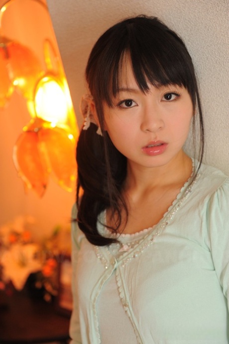 Nozomi Hazuki, japonesa totalmente vestida, segura o rosto firme em saia estampada.