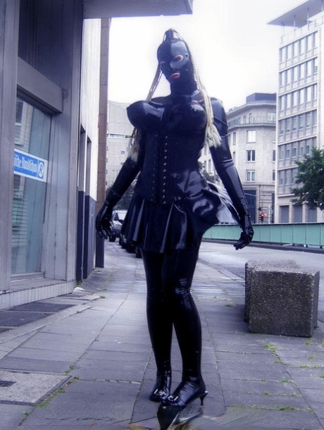 Blanke vrouw zwerft door openbare straten terwijl ze rubberen kleding draagt