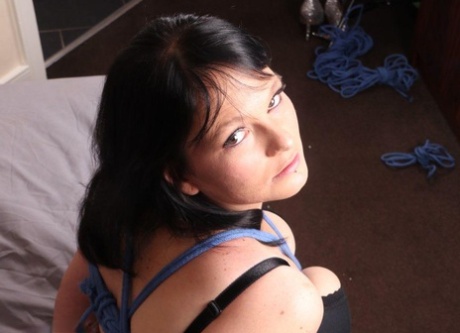 Lubben mørkhåret kvinne ligger fastbundet på en seng iført sexy strømpebukser