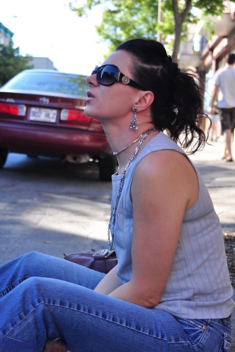 En brunette røyker en sigarett i en travel gate mens hun er fullt påkledd.