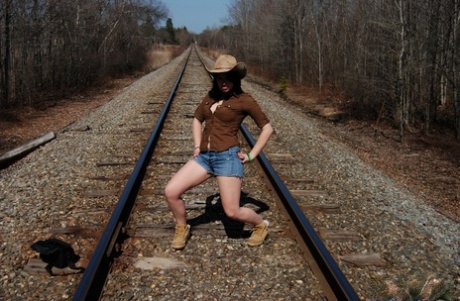 La giovane dilettante Emily Love si espone sui binari della ferrovia con cappello e stivali