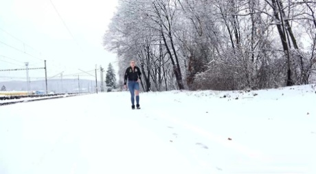 Blondes Mädchen Gianna Ray zieht zerrissene Jeans herunter, um auf schneebedeckten Boden zu pinkeln