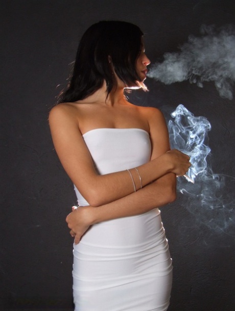 Ung brunette ryger en cigaret i stram hvid kjole og høje hæle