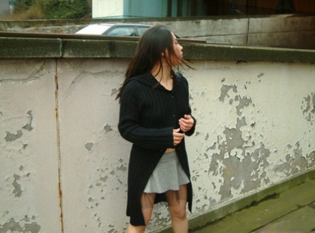 Asiatisk jente står naken i skjørt på et fortau i Storbritannia.